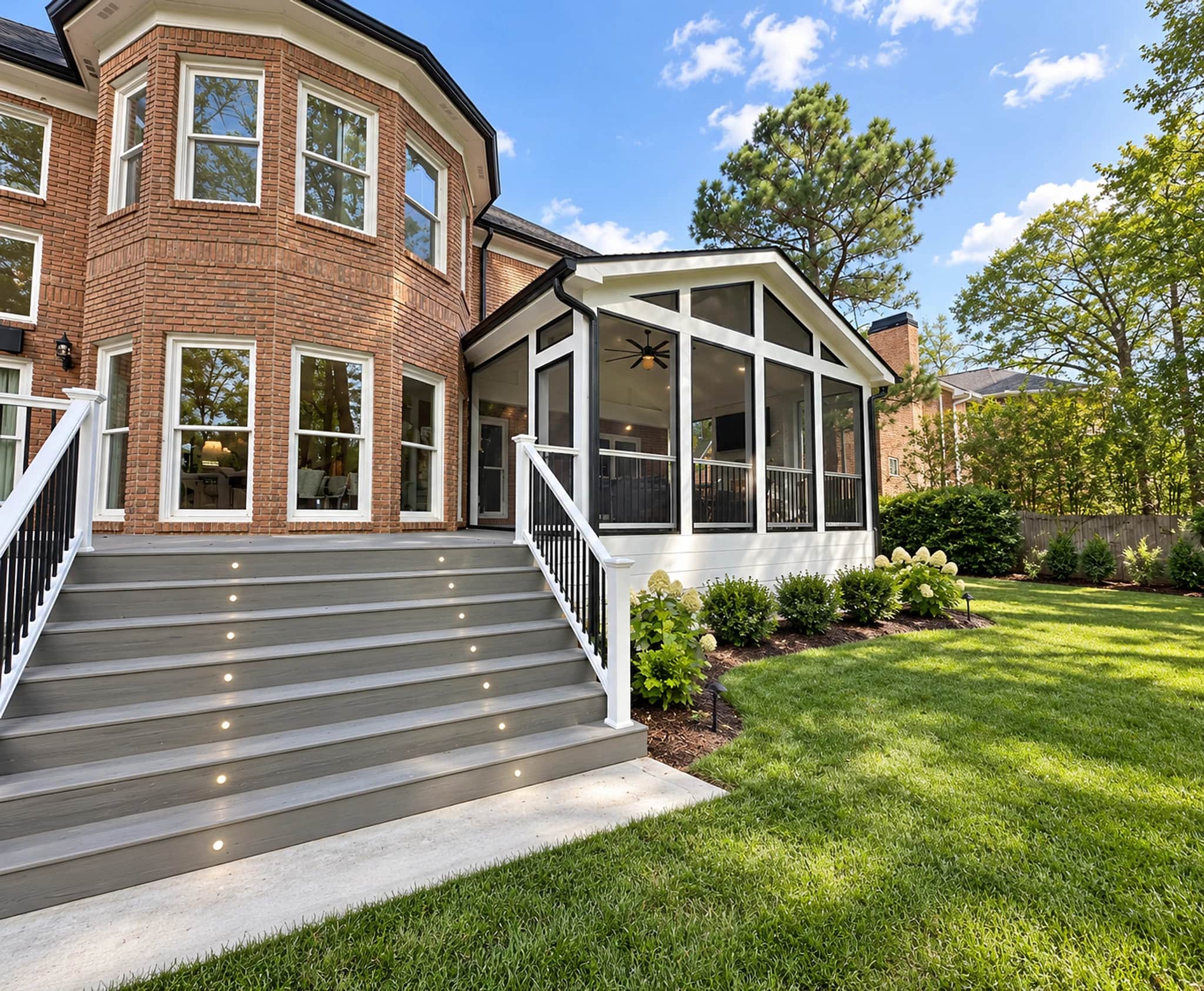 Screened porch addition on a brick two-story house, with a composite deck, lit stair risers and new planting beds