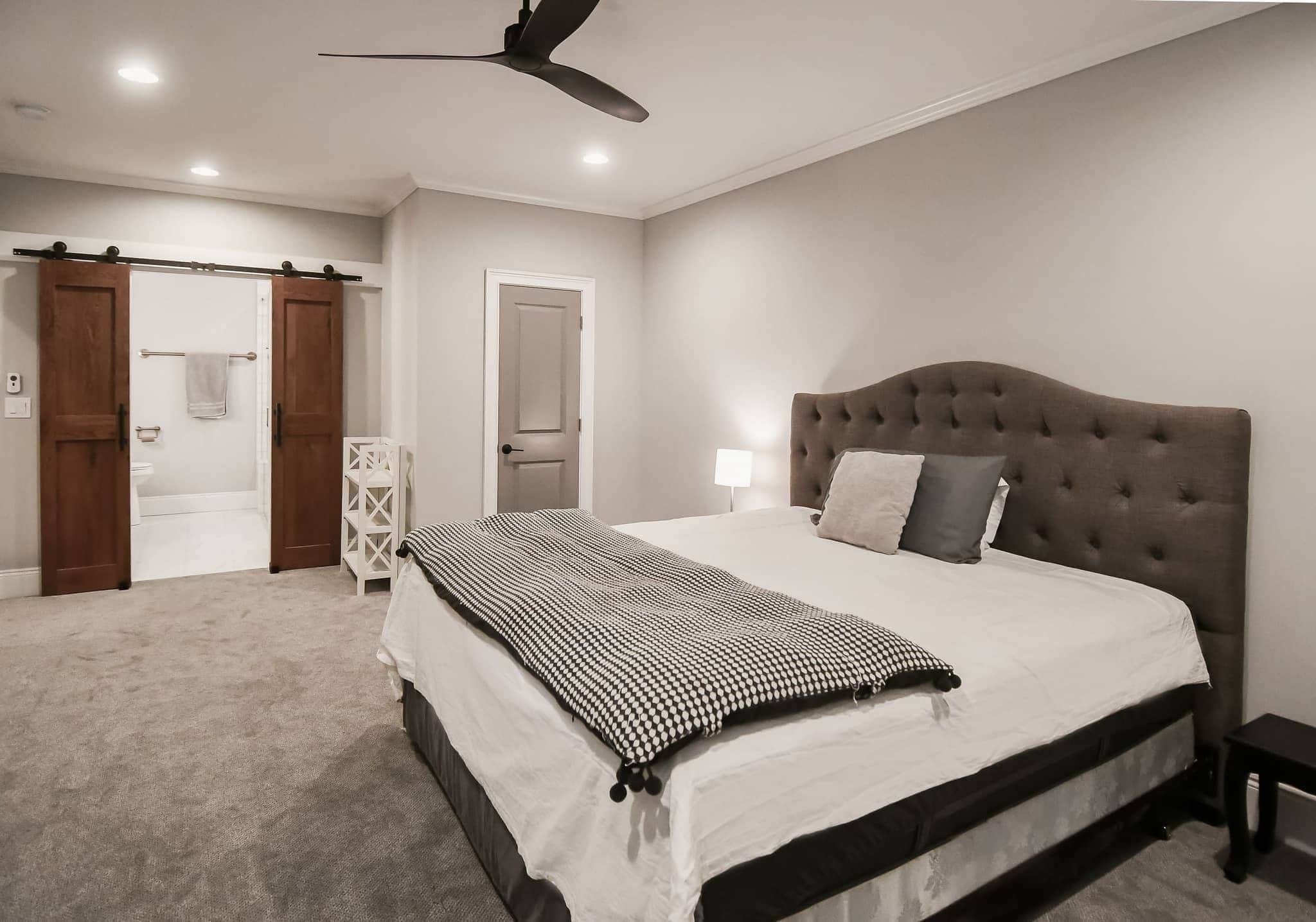 Finished basement bedroom suite with tufted headboard and sliding barn doors to a bath