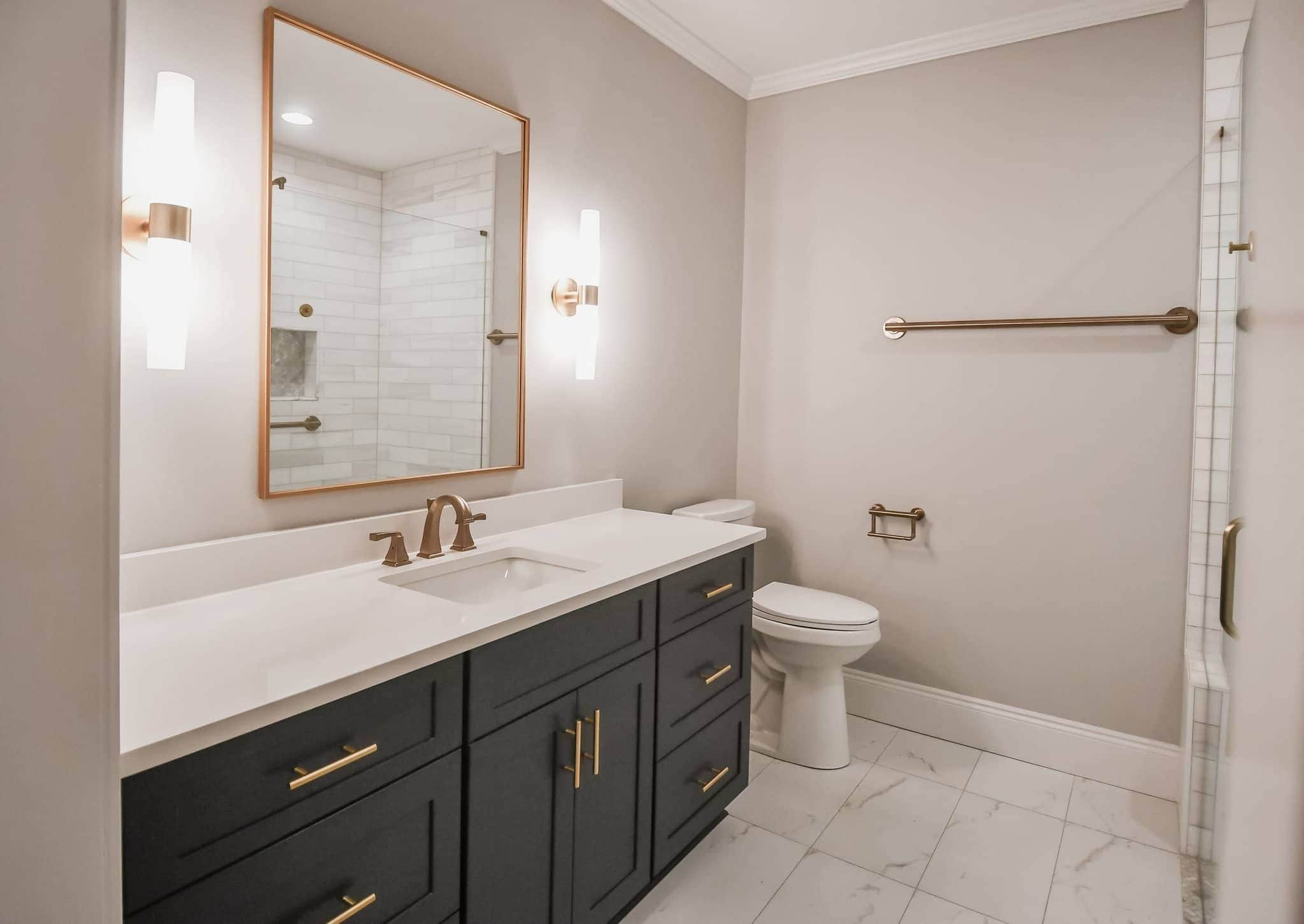 Bathroom with navy vanity, marble counter and brushed-gold mirror