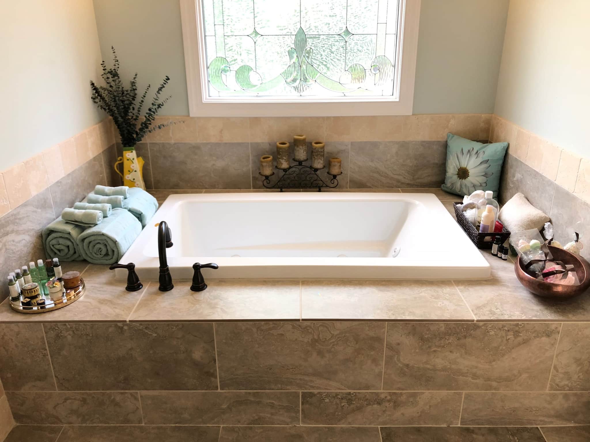 Drop-in soaking tub set into a tiled surround beneath a leaded-glass window