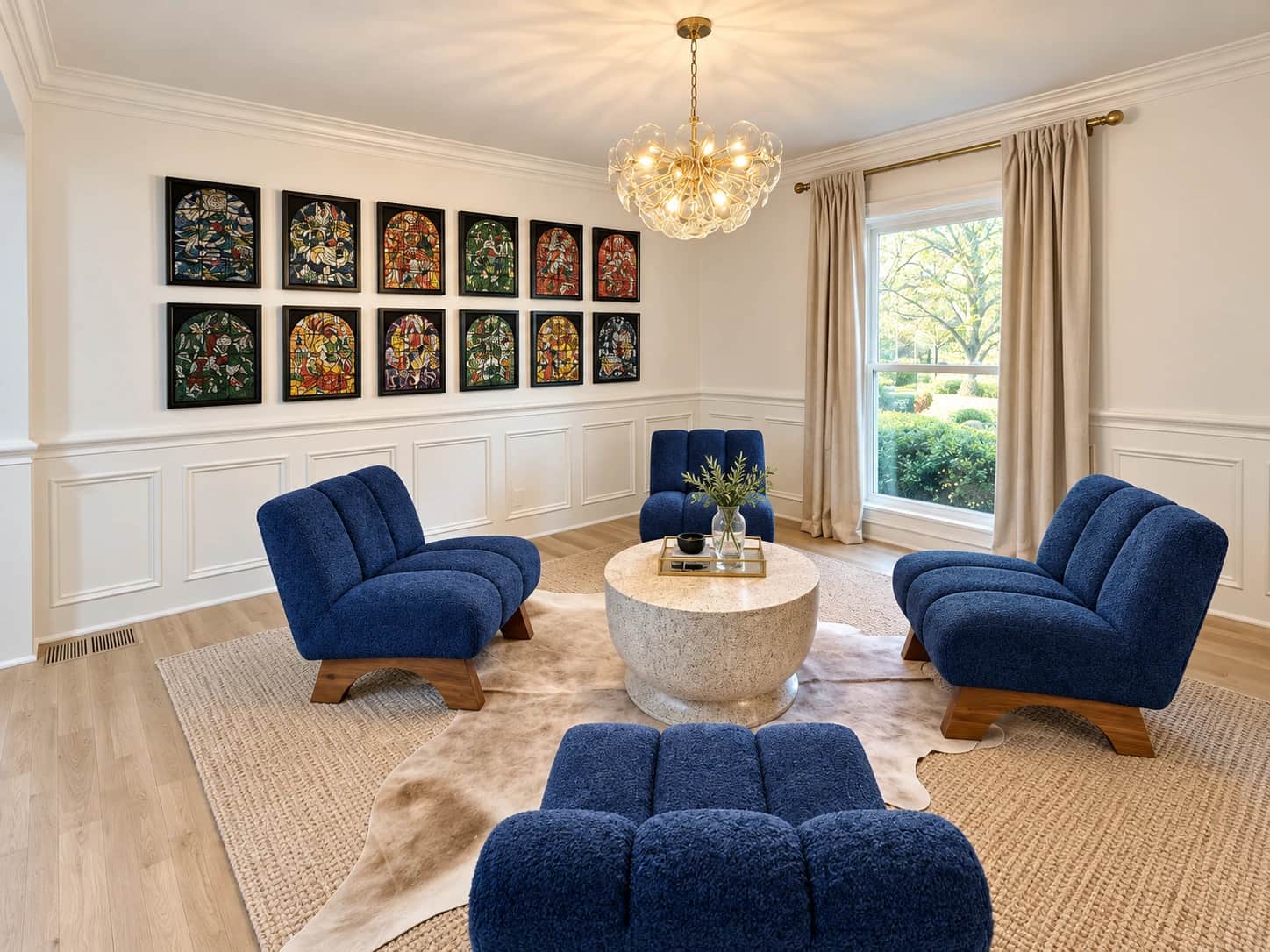 Formal sitting room with picture-frame wainscoting, a gallery wall of framed stained-glass panels and blue lounge chairs around a round stone table