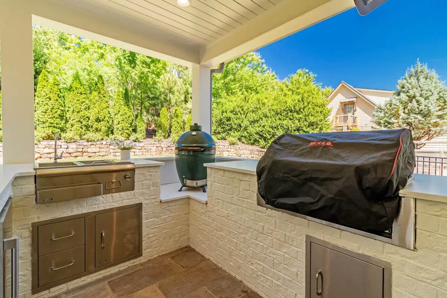 Built-in outdoor kitchen with stainless grill, green ceramic smoker and white brick base