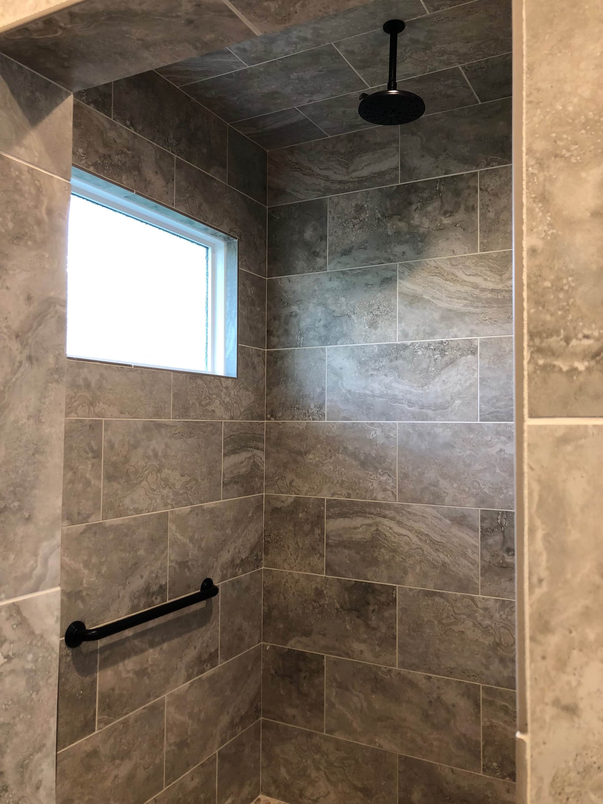 Curbless walk-in shower clad floor to ceiling in large-format stone tile with a rainfall head