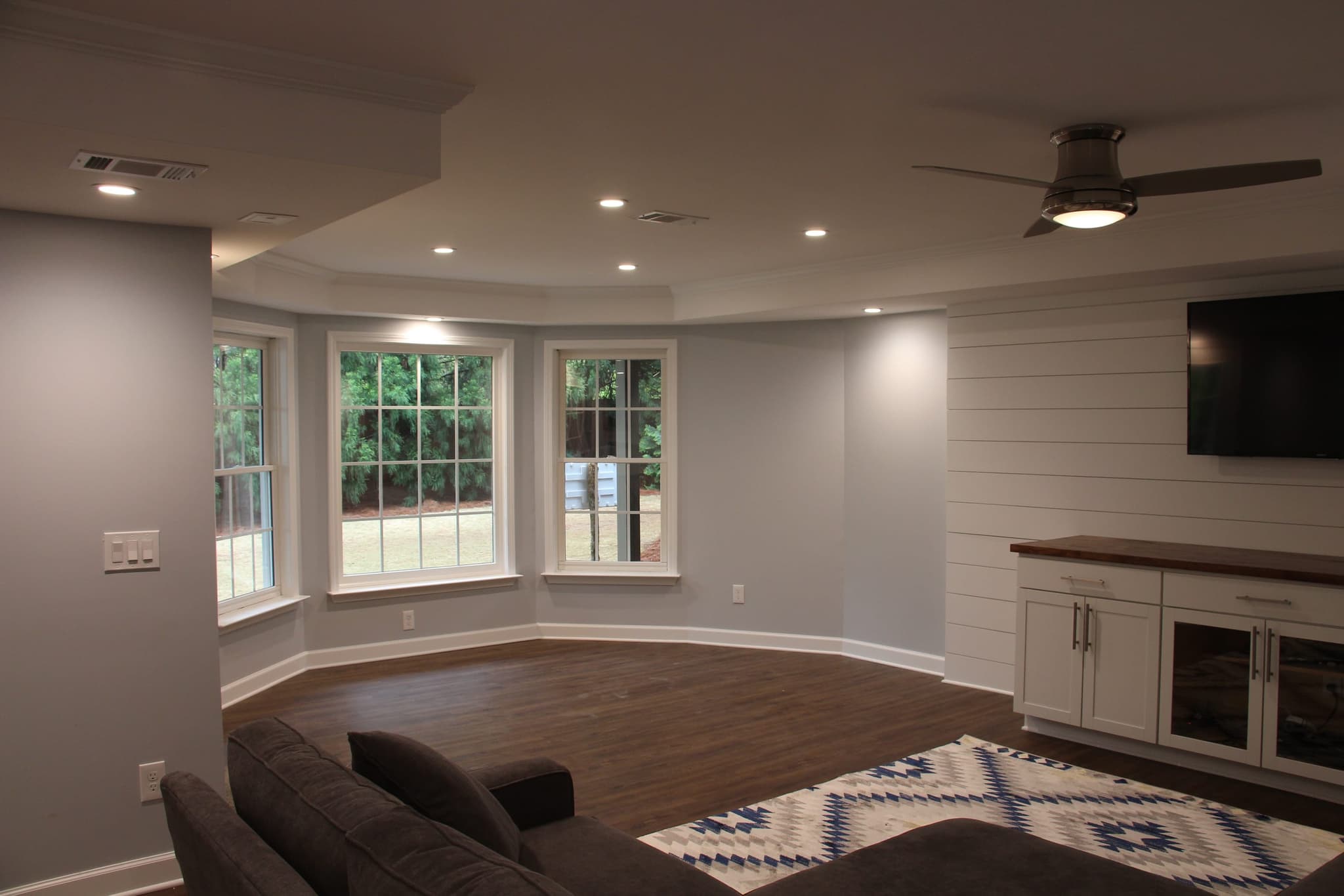 Finished basement living area with a window bay, shiplap accent wall and white built-ins under a butcher-block top