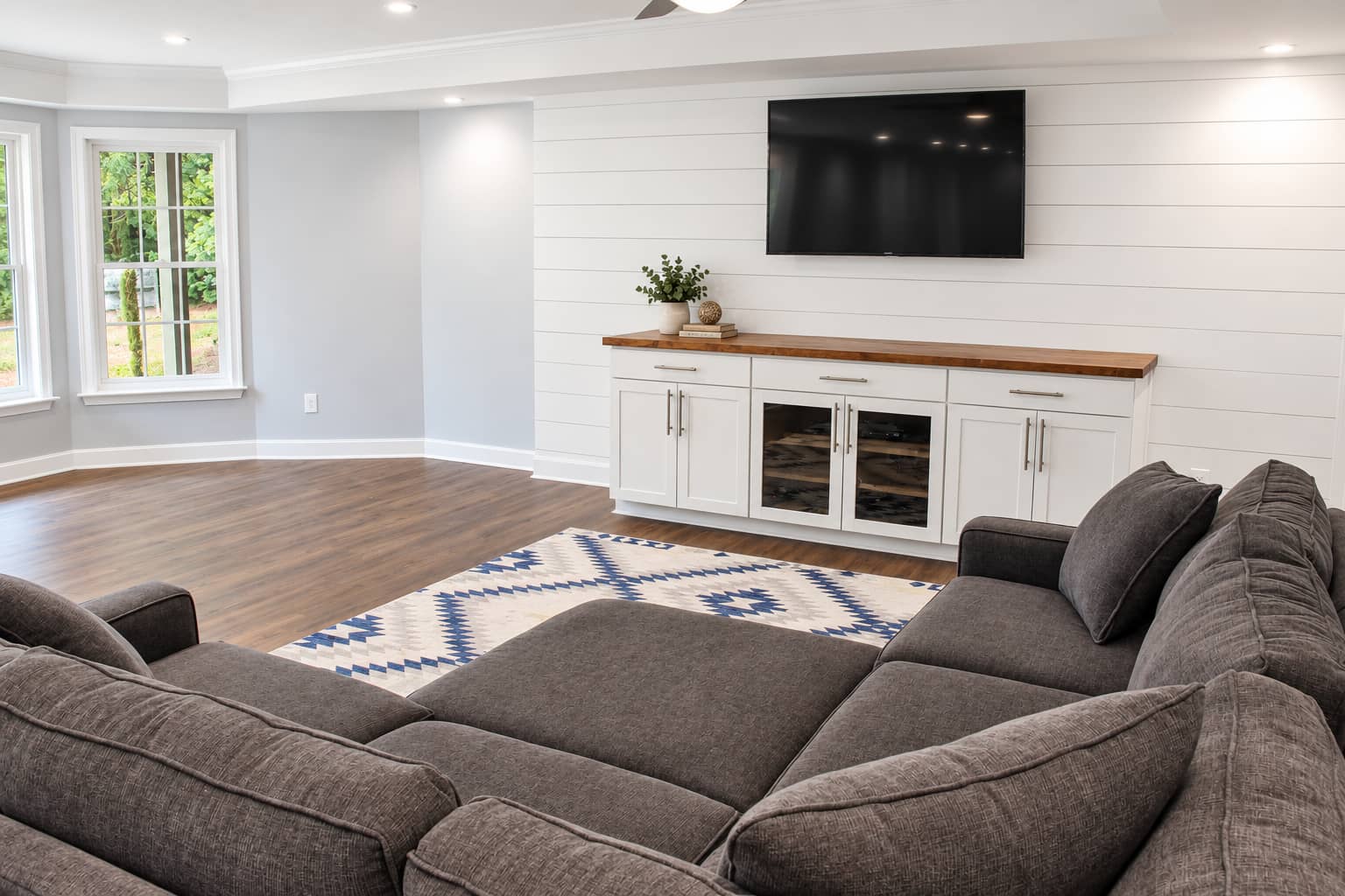 Media room with a wall-mounted television above a wine and beverage cabinet and a sectional facing it