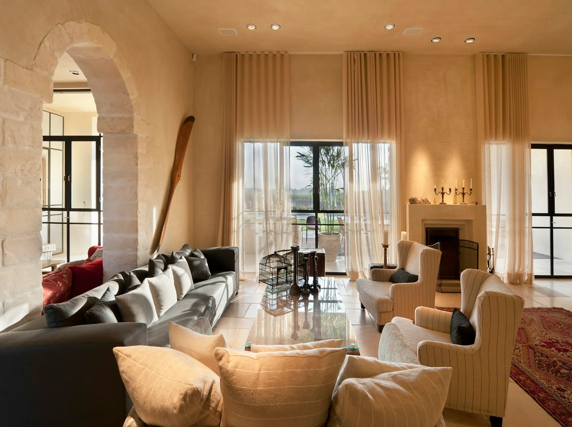 Great room with limestone walls, a stone arch, floor-to-ceiling sheers and a carved stone fireplace