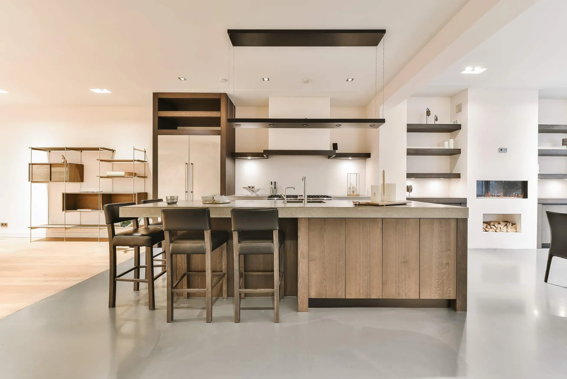 Open modern kitchen with a pale oak island, concrete-look counter, black floating shelves and leather barstools