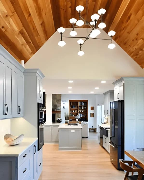 Open kitchen and living area under a vaulted wood-plank ceiling, with gray shaker cabinets, a center island and a globe chandelier