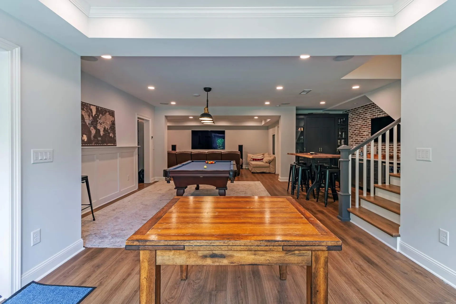 Wide finished basement with a pool table, a brick bar with a live-edge counter and a TV lounge