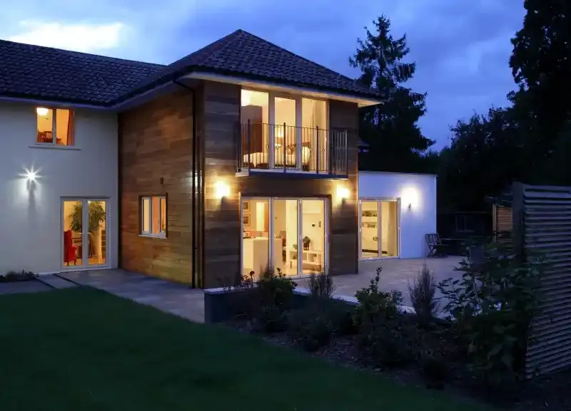 Modern two-story home at dusk with timber cladding, a balcony and lit bifold doors onto the patio
