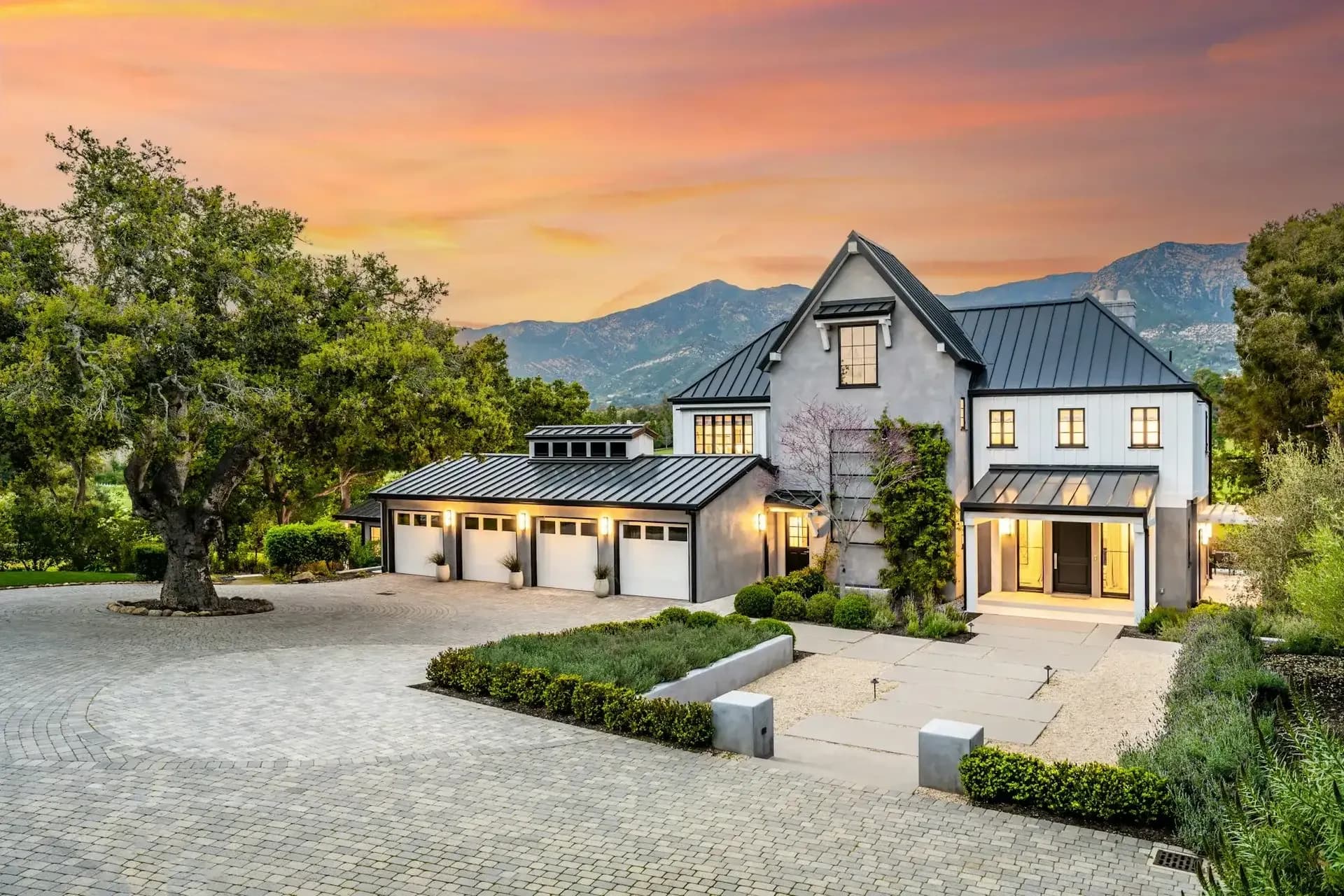 Custom home at sunset with board-and-batten siding, a standing-seam metal roof and a paver motor court