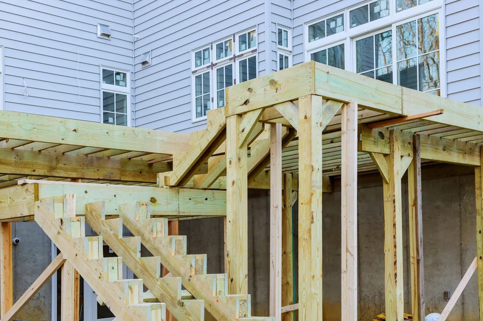 Raised deck and covered porch framing going up against a gray-sided home