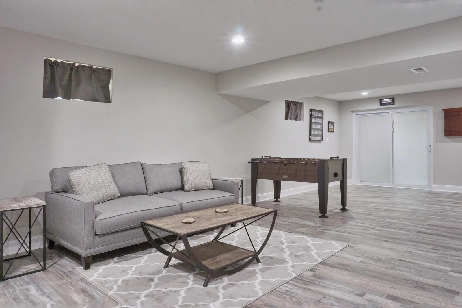 Finished basement living area with a gray sofa, a foosball table and wood-look plank flooring