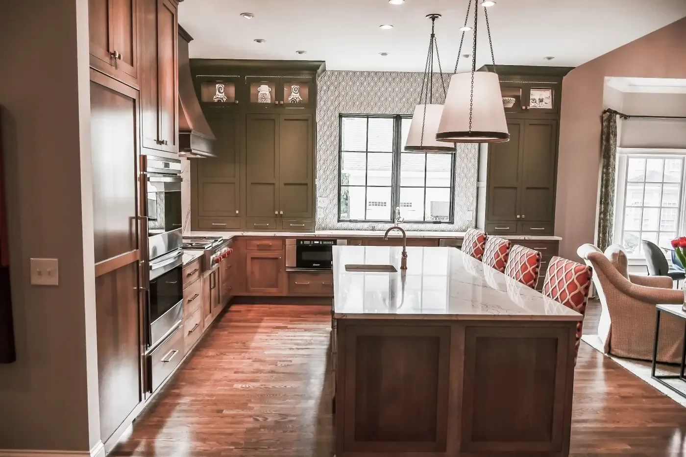 Kitchen with olive-green uppers, cherry base cabinets, a marble island and drum pendants