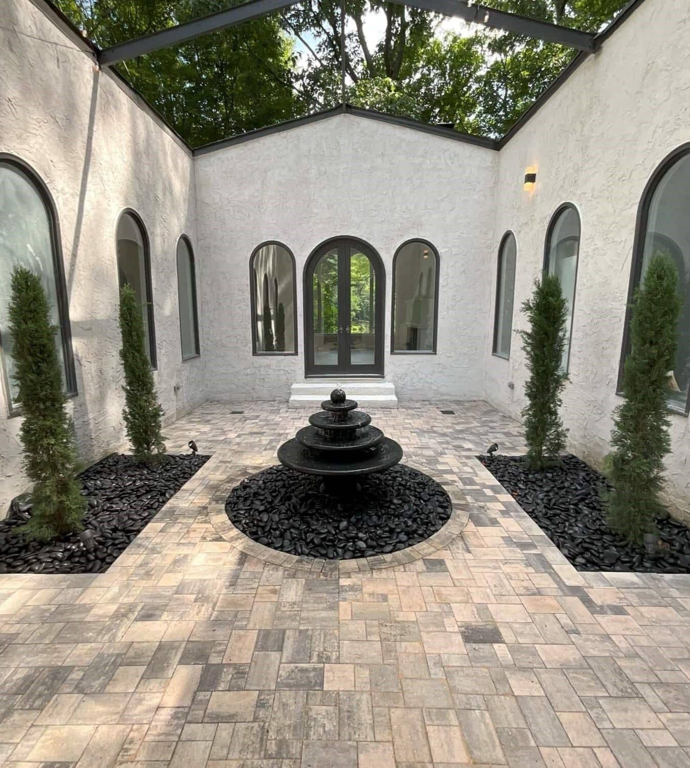 Stucco home addition forming a private courtyard with arched windows and a tiered black fountain