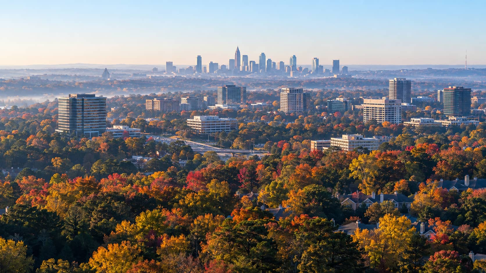 Aerial view over wooded Dunwoody rooftops in autumn toward the Atlanta skyline