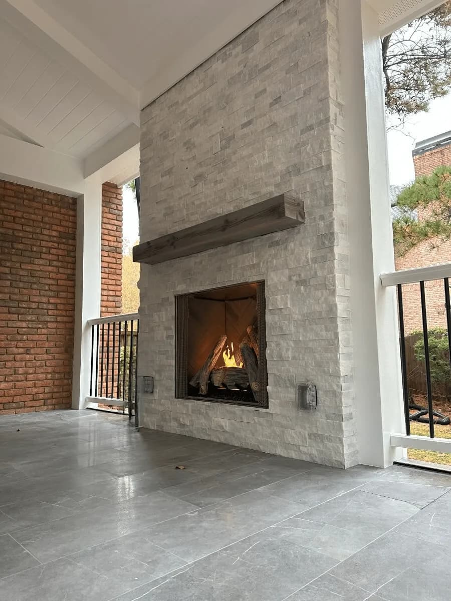 Covered outdoor patio with floor-to-ceiling stone gas fireplace and stained wood mantel
