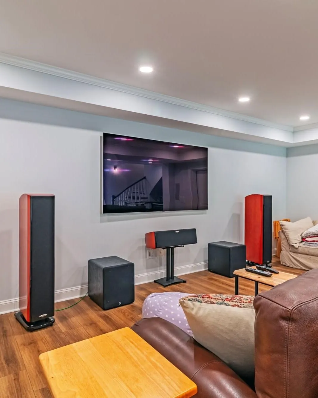 Finished basement media room with a wall-mounted TV, tower speakers and a leather sectional