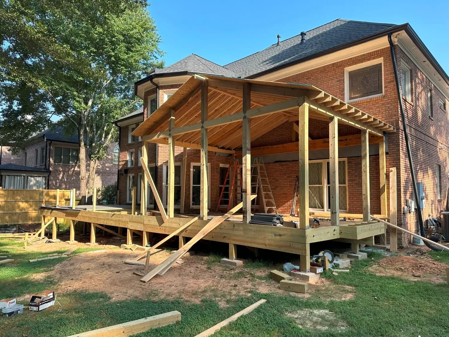 Covered porch and deck addition under framing at the back of a two-story brick home