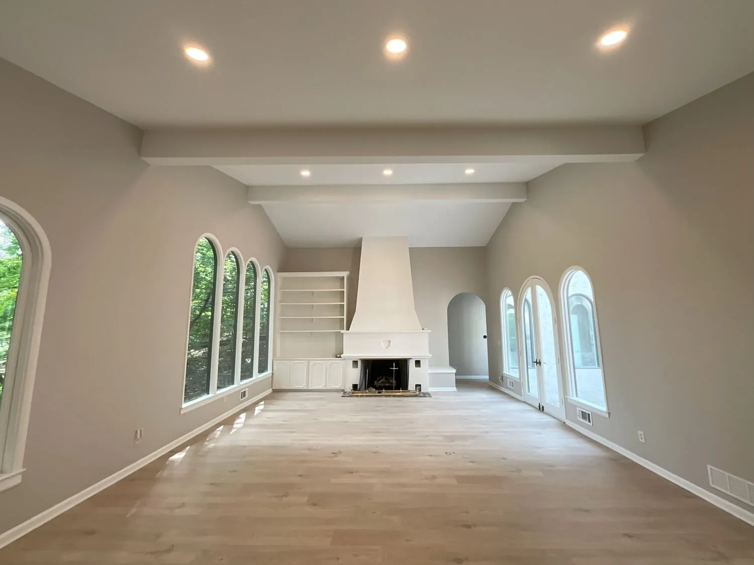 New great room addition with painted ceiling beams, a white stucco fireplace, built-in shelving and arched windows
