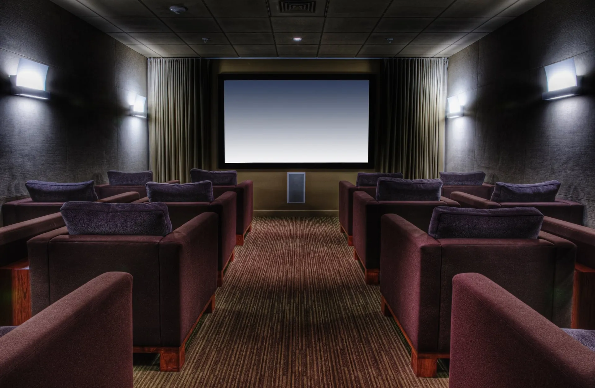 Basement home theater with tiered rows of plush armchairs and a curtained screen