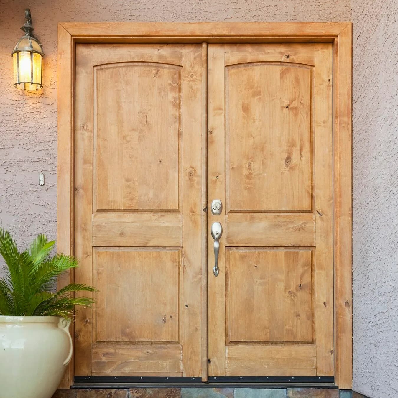 Knotty alder double entry doors on a stucco facade with a lantern sconce