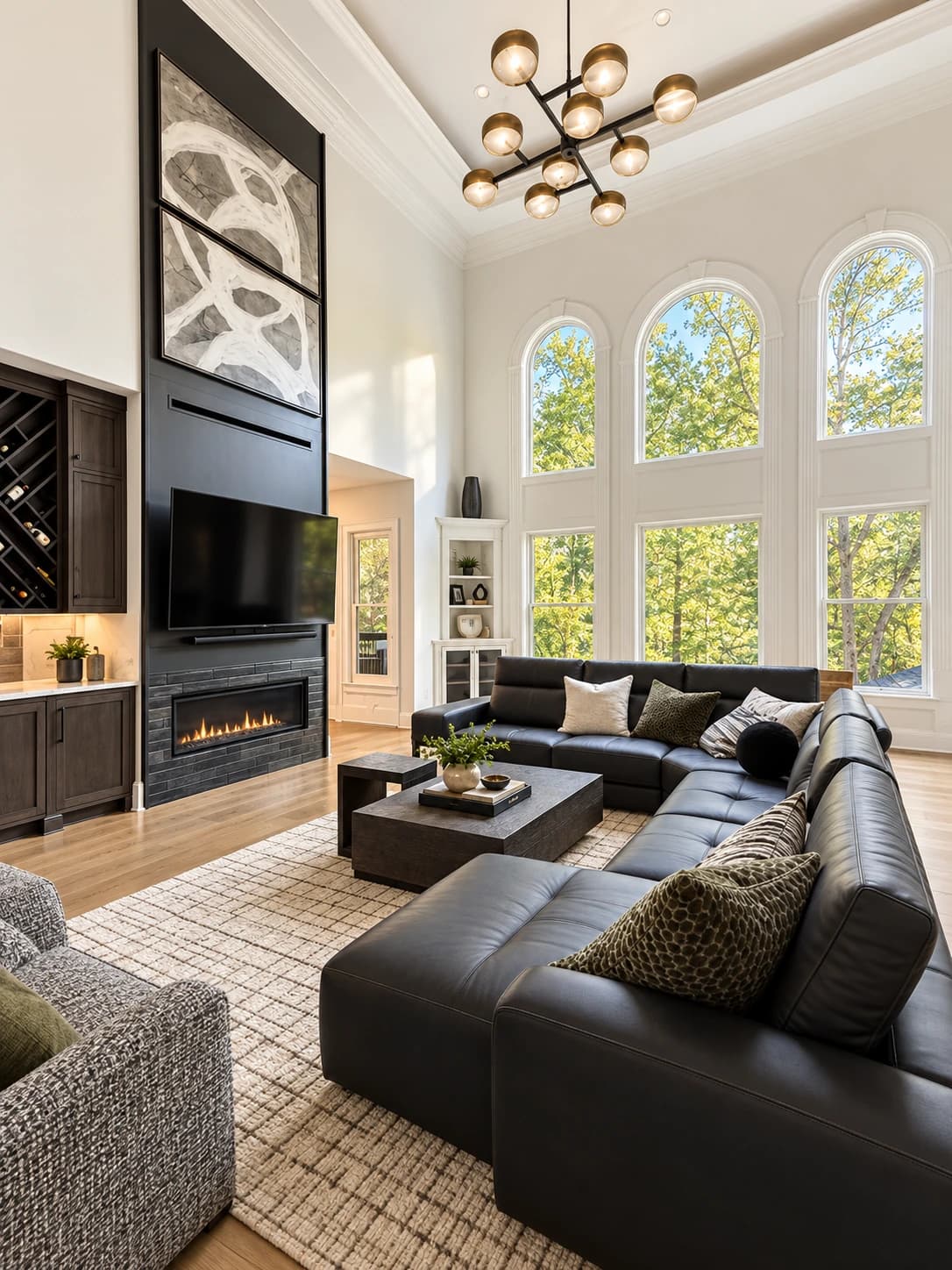 Two-story family room addition with a black floor-to-ceiling fireplace wall, a leather sectional and arched windows to the tree line