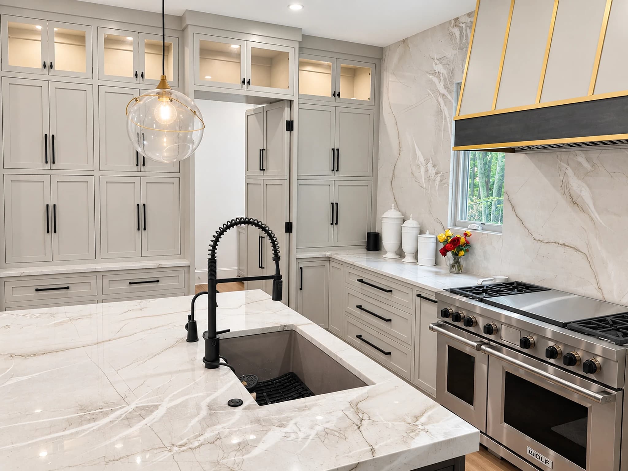 Remodeled kitchen with greige inset cabinetry, a marble-topped island, lit glass-front upper cabinets and a Wolf range under a brass-banded hood